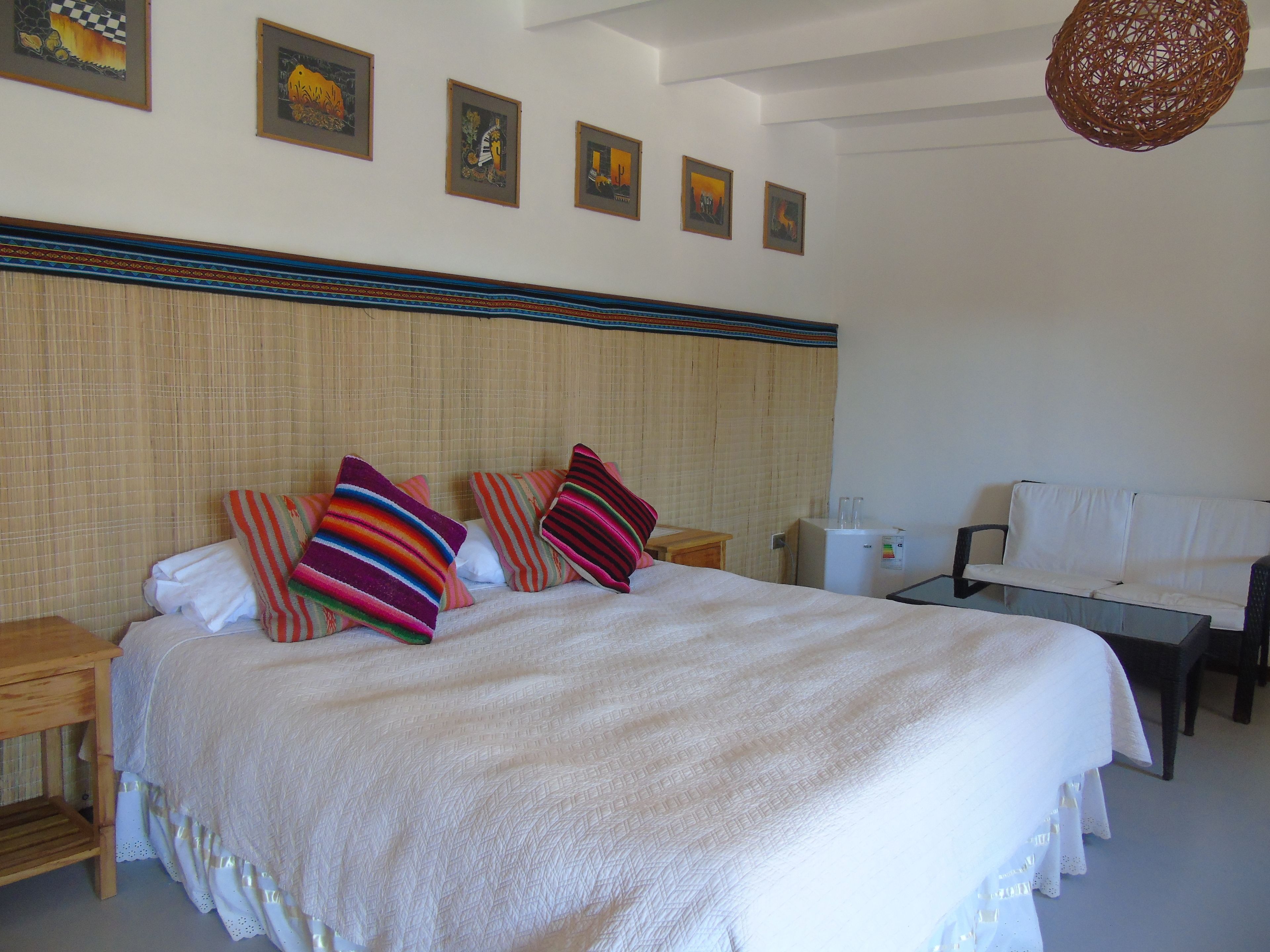 A neatly arranged hotel room with a large bed, a small table, a sofa, and a refrigerator.