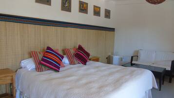 A neatly arranged hotel room with a large bed, a small table, a sofa, and a refrigerator.
