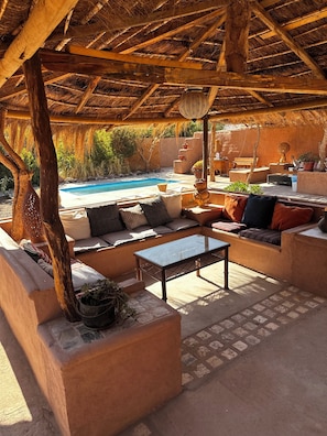 A covered outdoor seating area with a pool in the background.