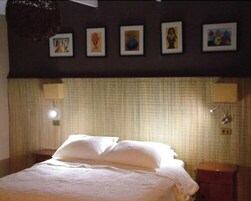 Una habitación de hotel con una cama, una mesita de noche, una lámpara y una pared decorada con cuadros.