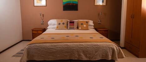 A double bed with a floral bedspread, two bedside tables, a nightstand, and a wardrobe.