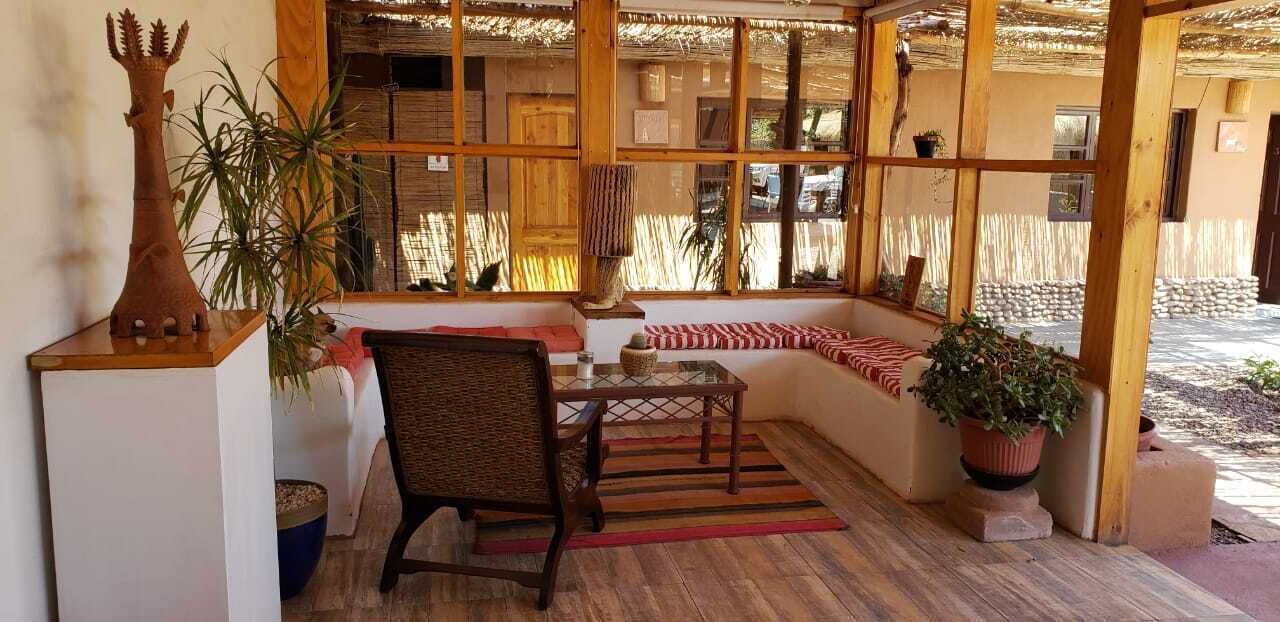 Un patio acogedor con una silla de mimbre, una mesita y un banco. Hay plantas en macetas y una escultura decorativa sobre un pedestal.