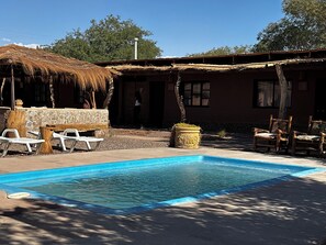 A pool area with lounge chairs, a stone bench, and a rustic building with a thatched roof. - Pat'ta Hoiri Hotel (San Pedro de Atacama)