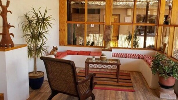 A cozy living room with a sofa, a chair, a small table, and a large window with wooden frames. - Pat'ta Hoiri Hotel (San Pedro de Atacama)