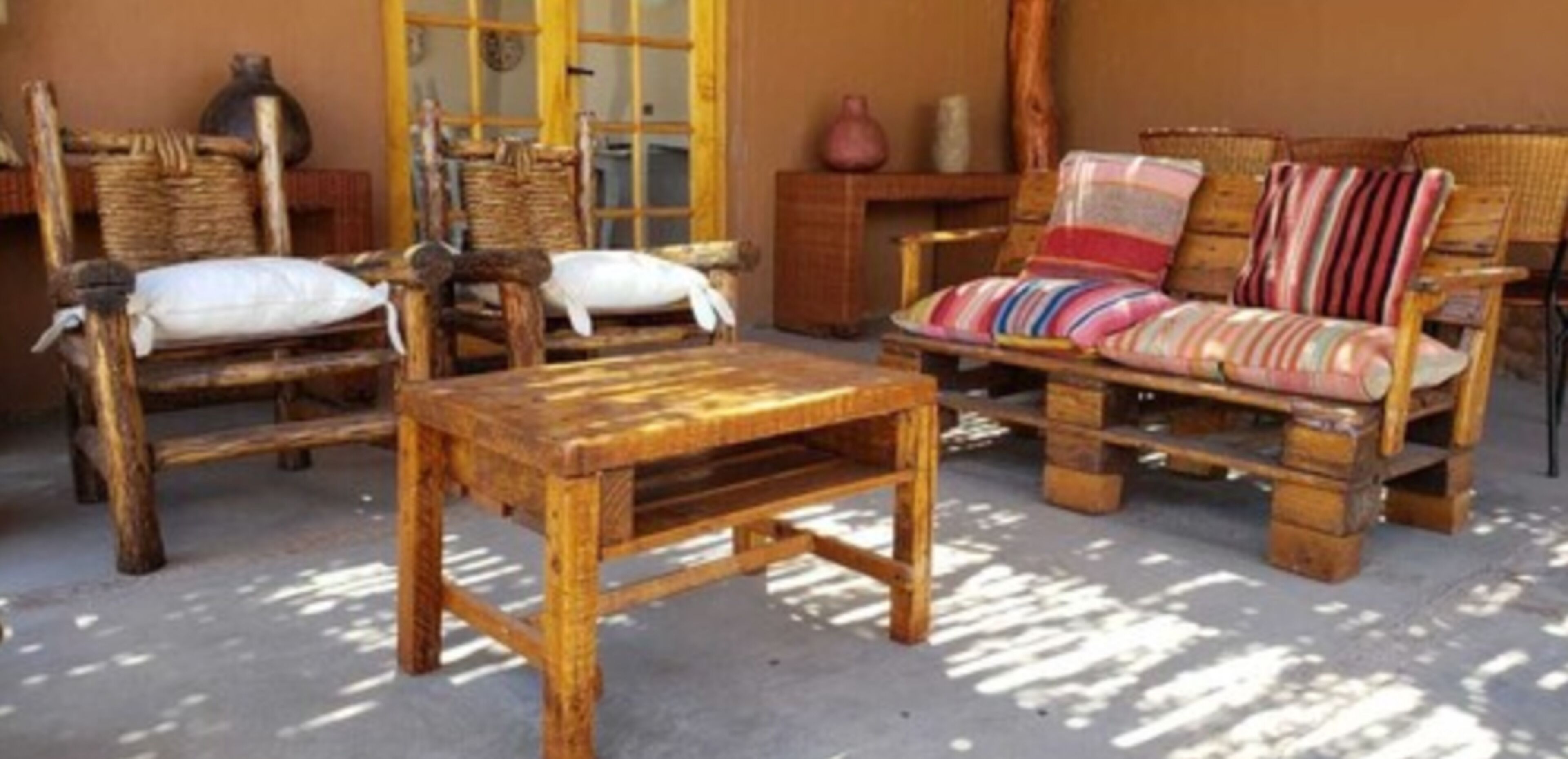 A rustic room with wooden furniture including a sofa and chairs, a small wooden table, and a window with a view.