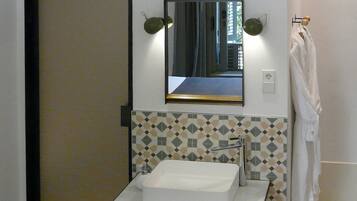 A bathroom with a rectangular sink, a mirror with a gold frame, and a patterned tile backsplash.
