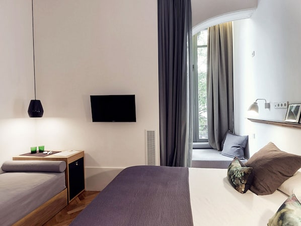 A modern hotel room with a bed, bedside table, TV, and a window with curtains. - Casa Mathilda (Barcelona)