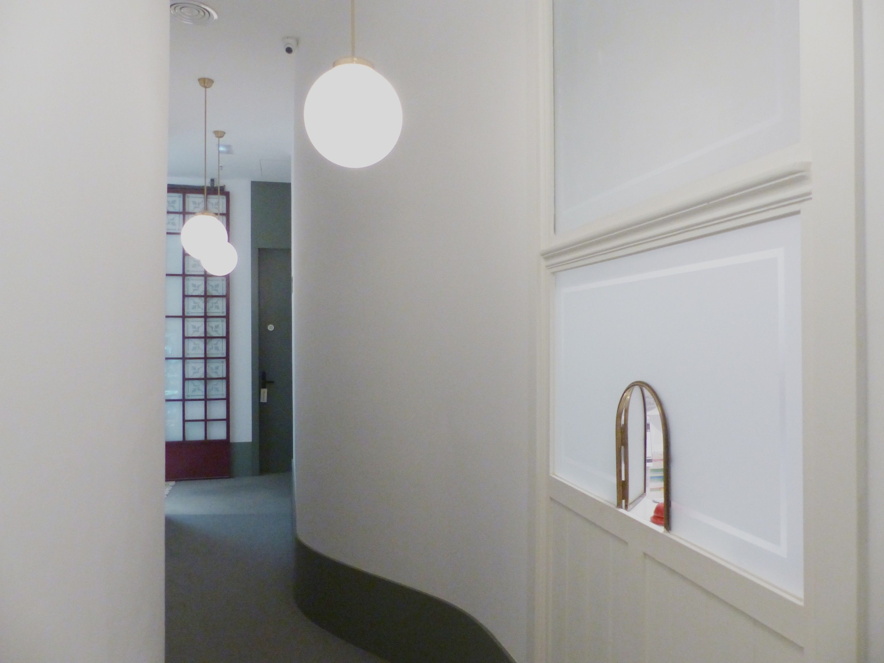 A hallway with a white wall, a round light fixture, and a window with a mirror.