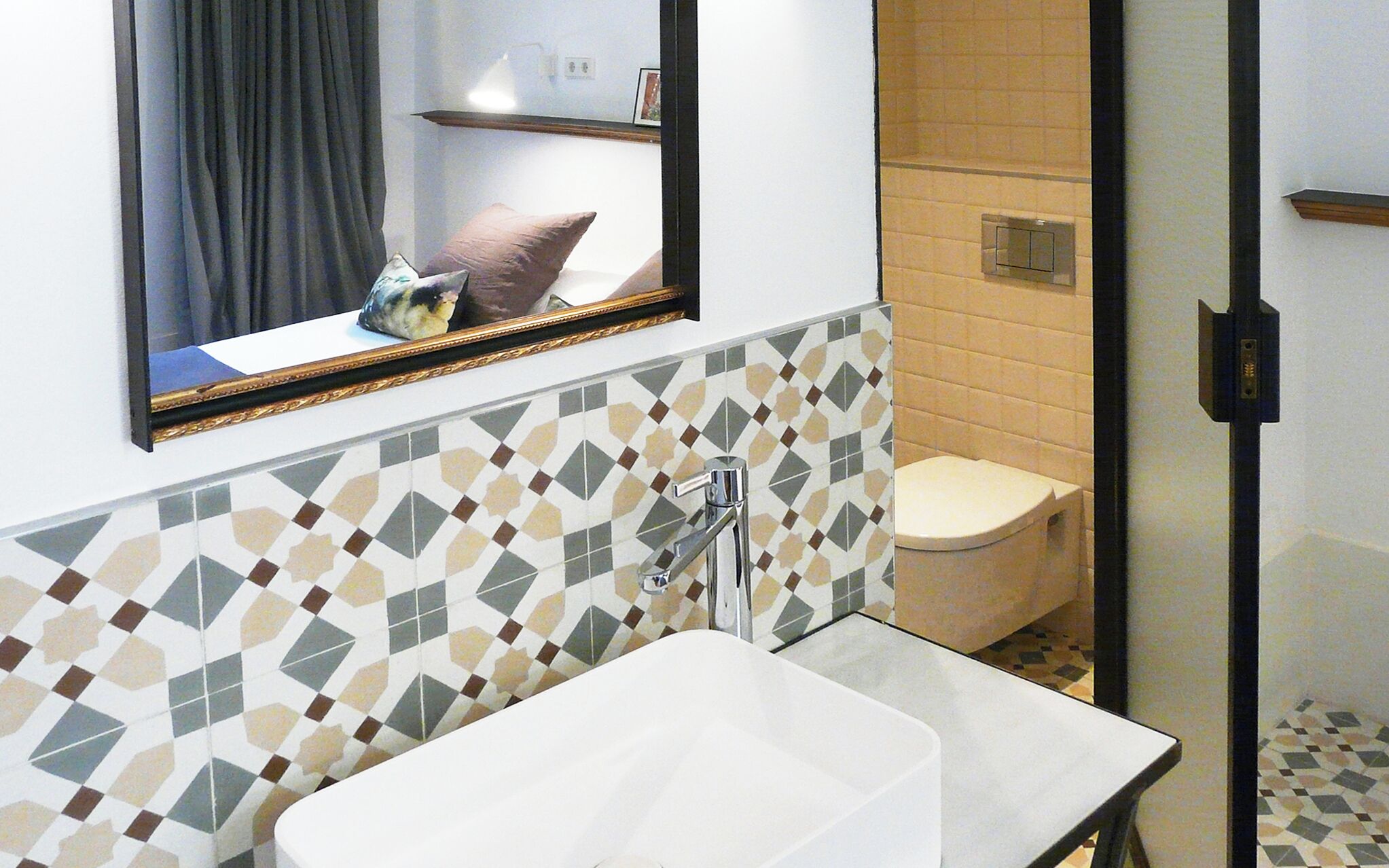 Un baño con lavamanos blanco, un espejo con marco dorado y un inodoro.