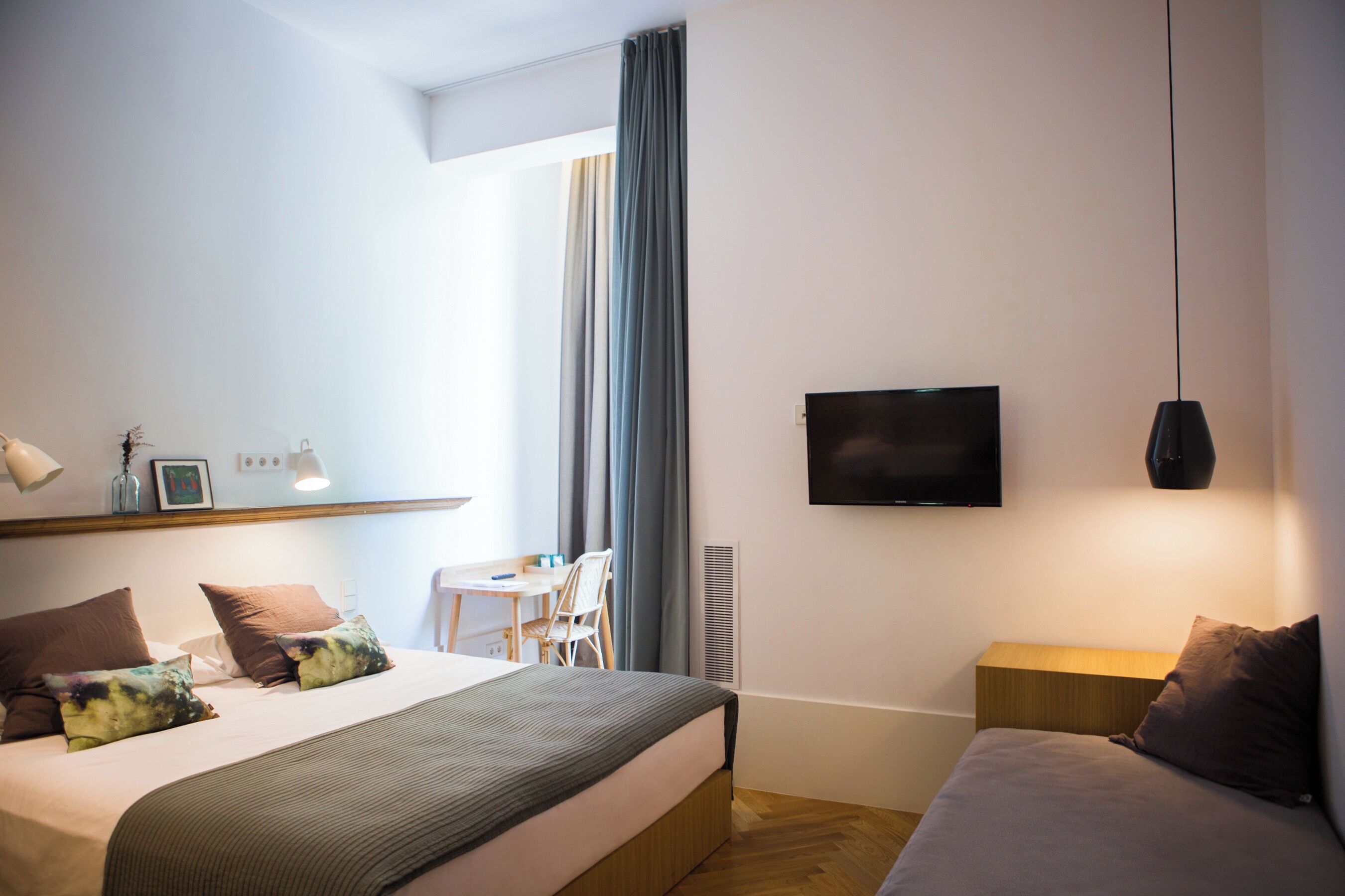 Une chambre d’hôtel comprenant un lit, une table de chevet, une télévision et un bureau avec une chaise.