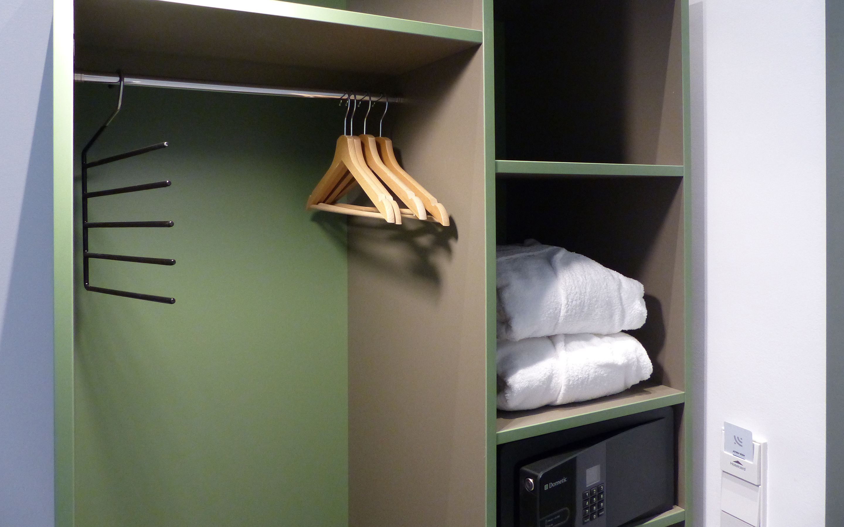 Un armario con puerta verde, perchas de madera y una toalla blanca doblada en un estante.