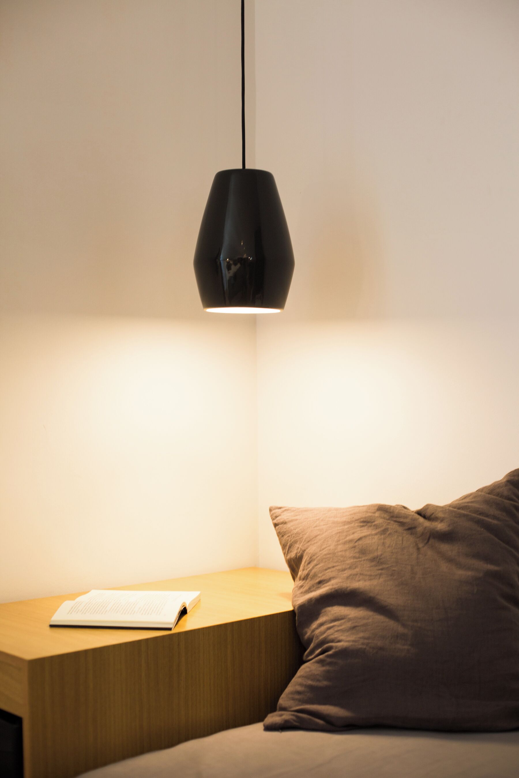 Una cama bien hecha con un almohadón y una mesita de noche con un libro.