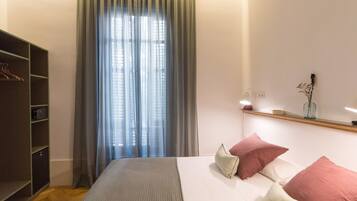 Een slaapkamer met een bed, een kledingkast, een raam met gordijnen en een nachtkastje met een vaas.