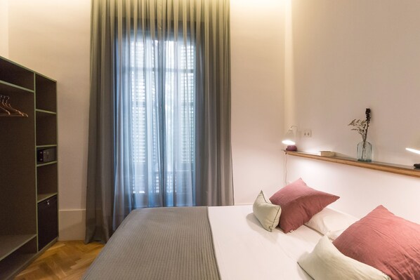 A bedroom with a bed, a wardrobe, a window with curtains, and a bedside table with a vase.