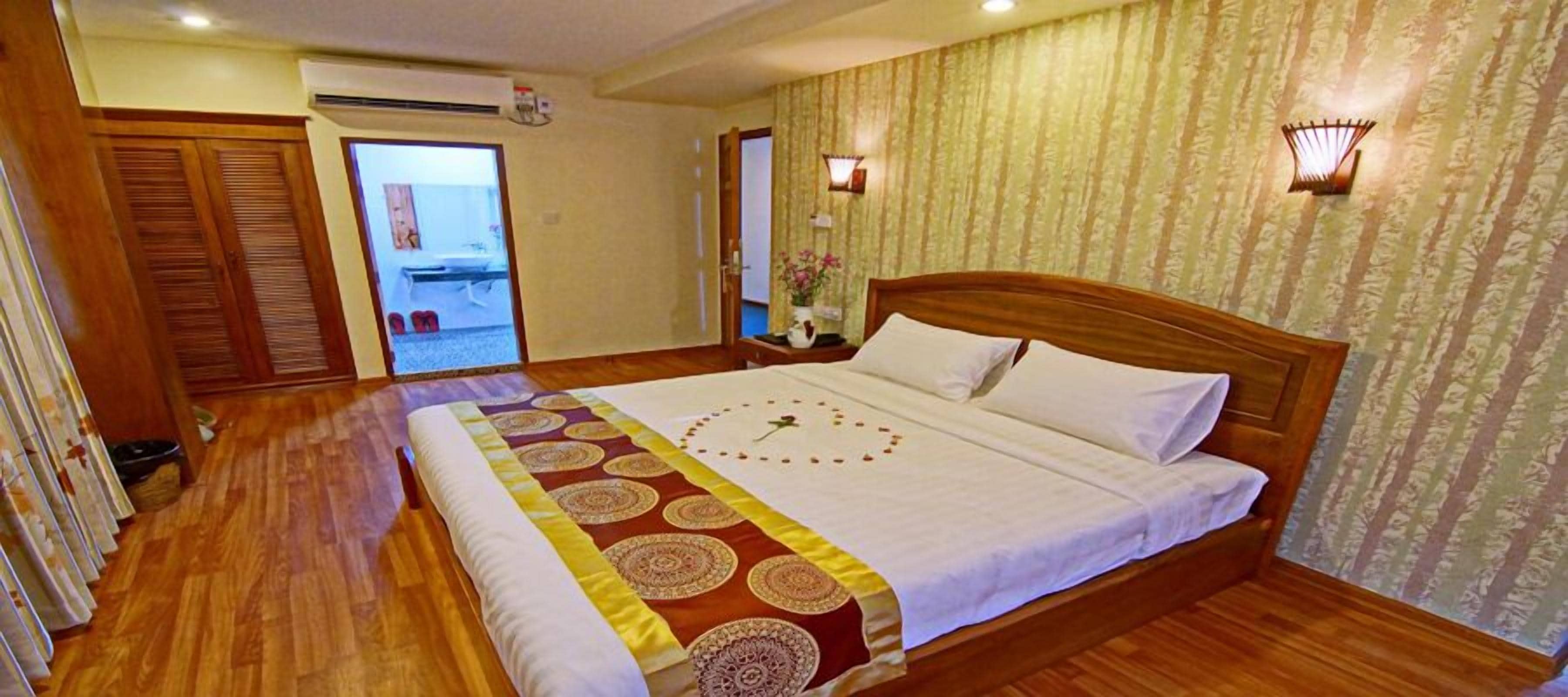 Una cama grande con una colcha estampada, cabecero de madera y dos lámparas de noche.