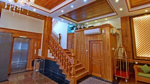 A wooden staircase with a chandelier, a wooden elevator, and a cushioned bench. - Royal Pearl Hotel (Mandalay)
