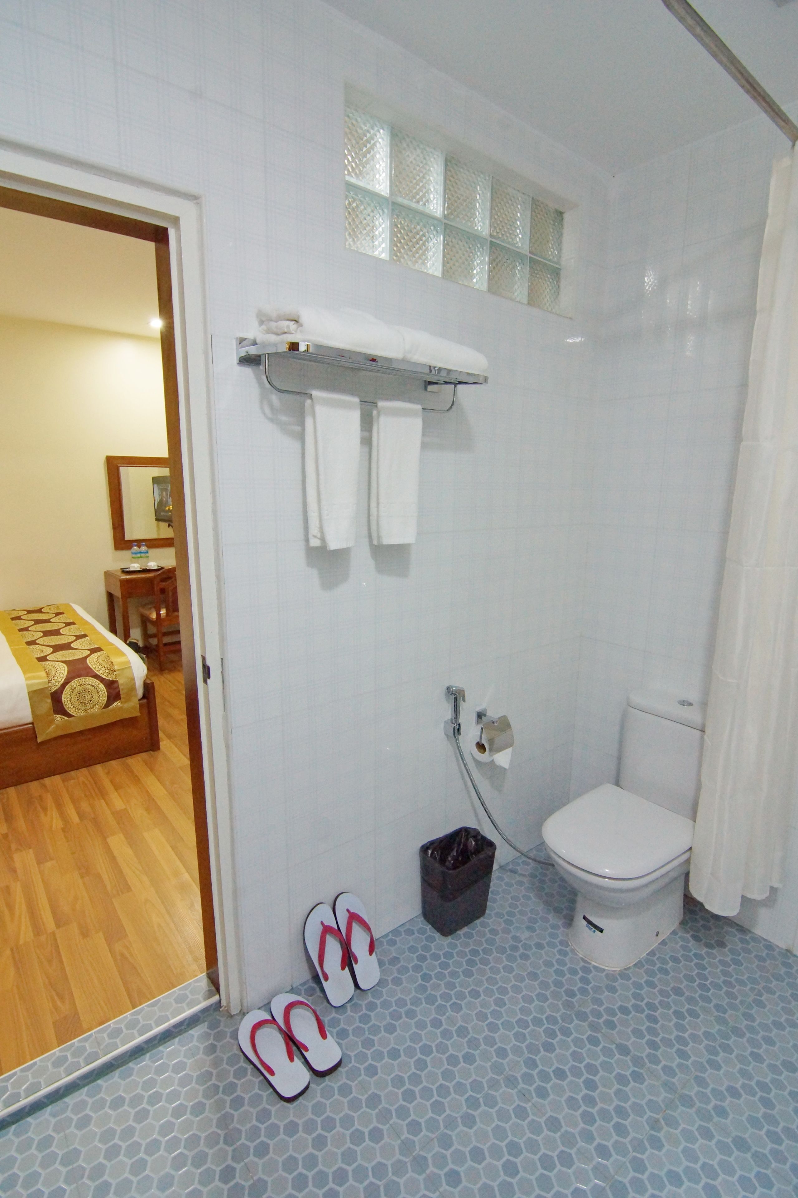 Un baño con inodoro, ducha y lavamanos. Hay un par de chanclas en el suelo.