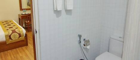 Un baño con inodoro, ducha y lavamanos. Hay un par de chanclas en el suelo.