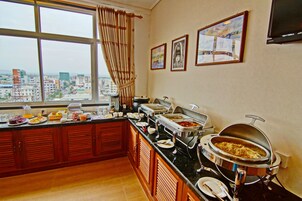 Montaje de bufé con varias estaciones de comida, un ventanal con vista a la ciudad y obras de arte en la pared.