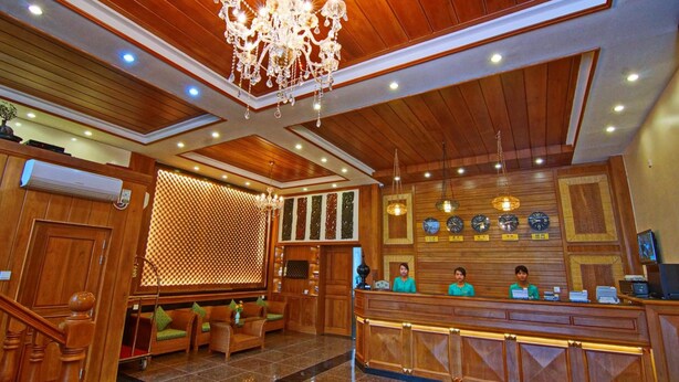 A hotel lobby with a wooden reception desk, seating area, and a chandelier. - Royal Pearl Hotel (Mandalay)