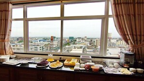 A breakfast buffet with various food items and a city view through large windows. - Royal Pearl Hotel (Mandalay)