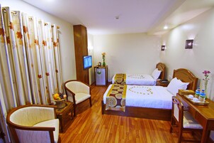 A hotel room with two beds, a TV, a desk with a tray of toiletries, and a chair.