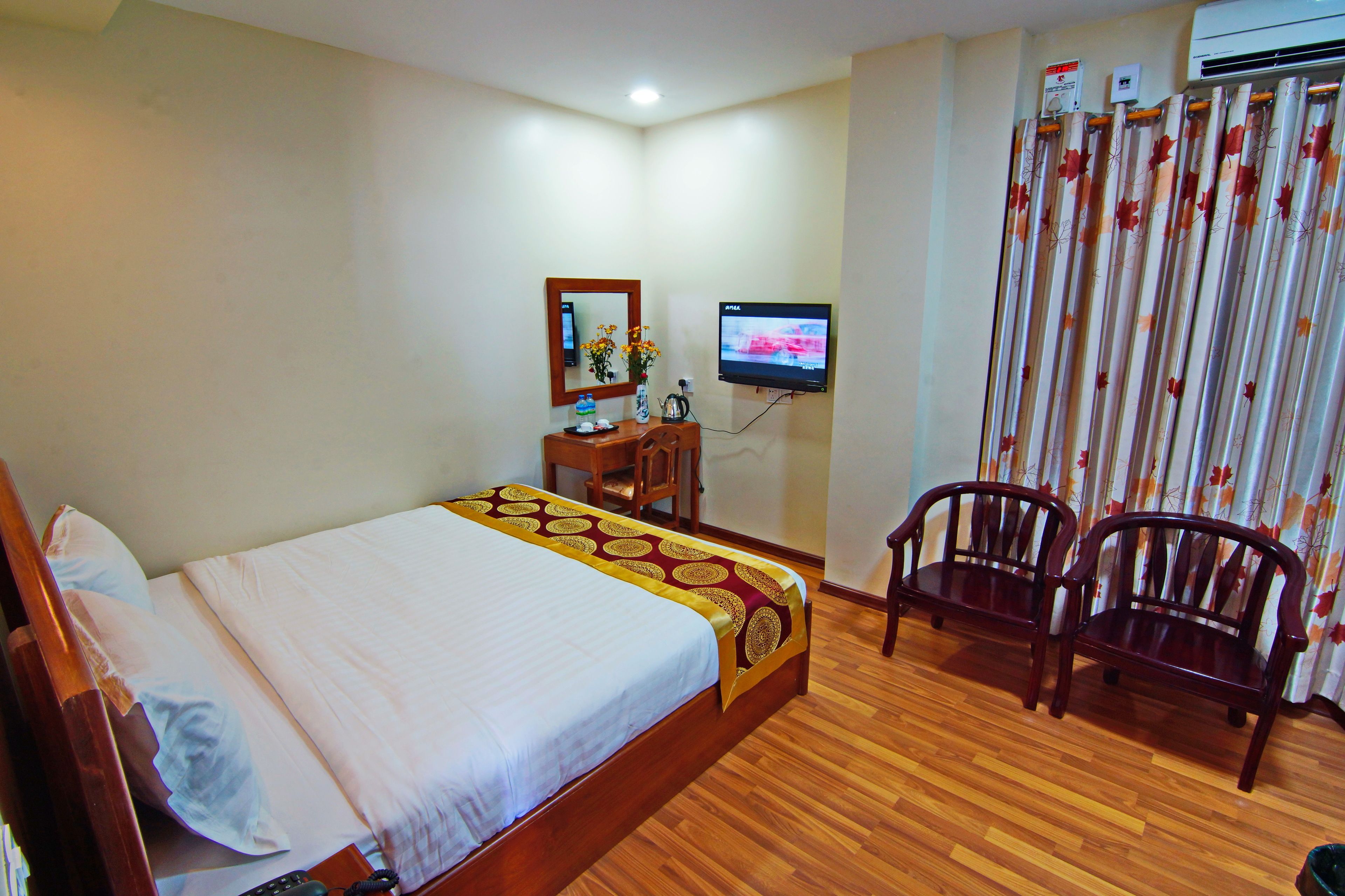 A hotel room with a wooden bed, a desk with a chair, a television, and a curtain with a floral pattern.