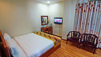 A hotel room with a wooden bed, a desk with a chair, a television, and a curtain with a floral pattern.