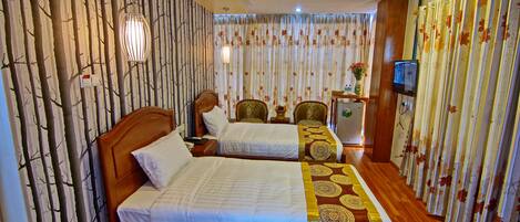 Quarto de hotel com duas camas, uma cabeceira de madeira, uma televisão e piso de madeira.