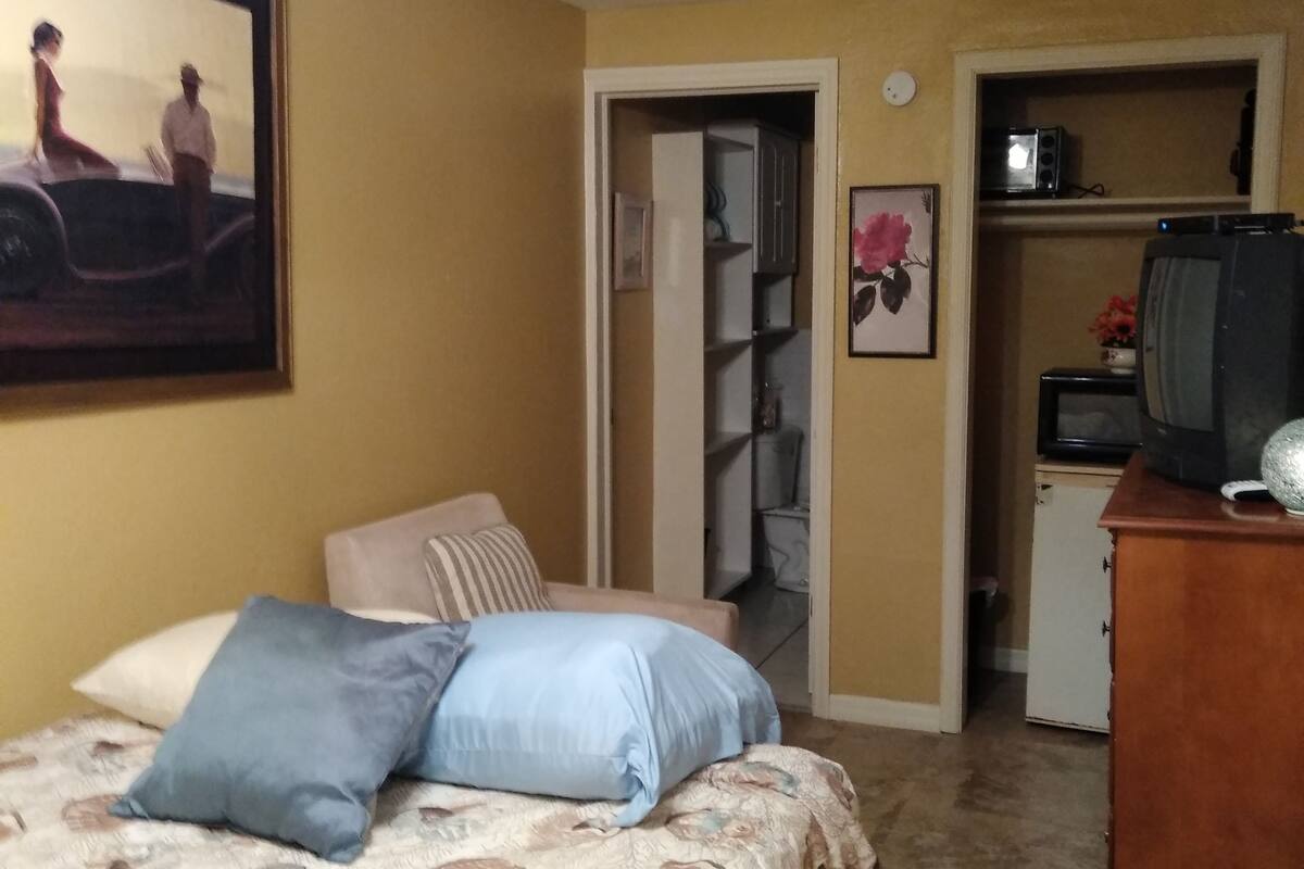 A bedroom with a bed, a dresser, a television, and a door leading to a bathroom.