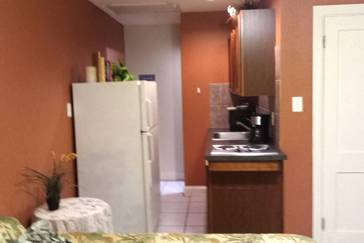A compact hotel room with a bed, a small kitchenette, a refrigerator, and a door leading to another room.