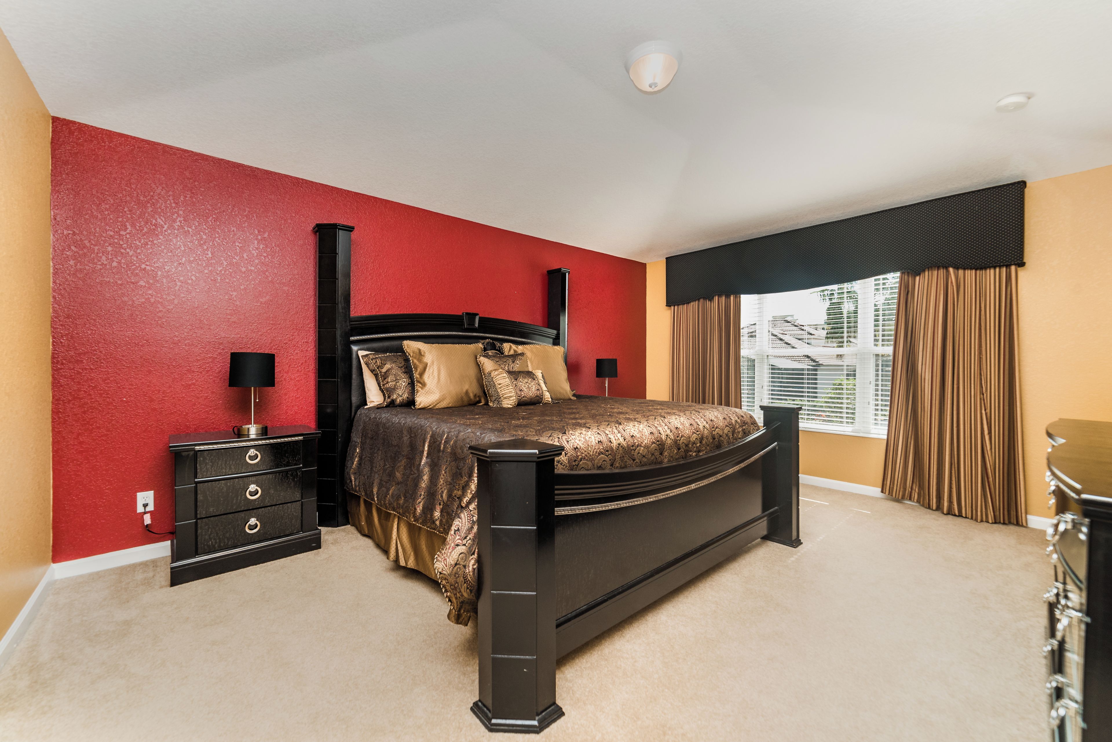 A bedroom with a bed, nightstands, a dresser, and a window with curtains.