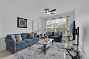 Un salon avec un canapé bleu, une table basse, un téléviseur et un ventilateur de plafond.