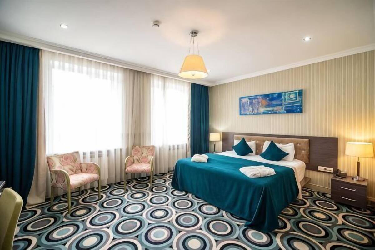 A hotel room with a bed, two chairs, a desk, a lamp, and a painting on the wall.