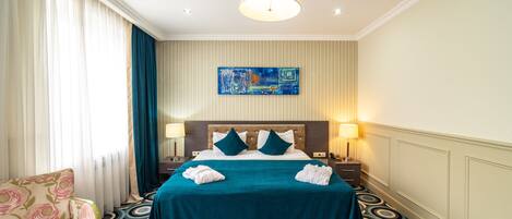 Habitación de hotel con una cama grande, dos lámparas de noche, un cabecero, un cuadro en la pared, una alfombra estampada y una silla.