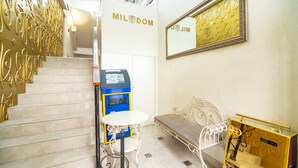 Et hotel lobby med en marmortrappe, en kiosk til selvbetjening, et hvidt bord, en bænk og et spejl monteret på væggen.