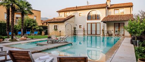 A pool area with lounge chairs, a stone building with a tiled roof, and a clear pool.