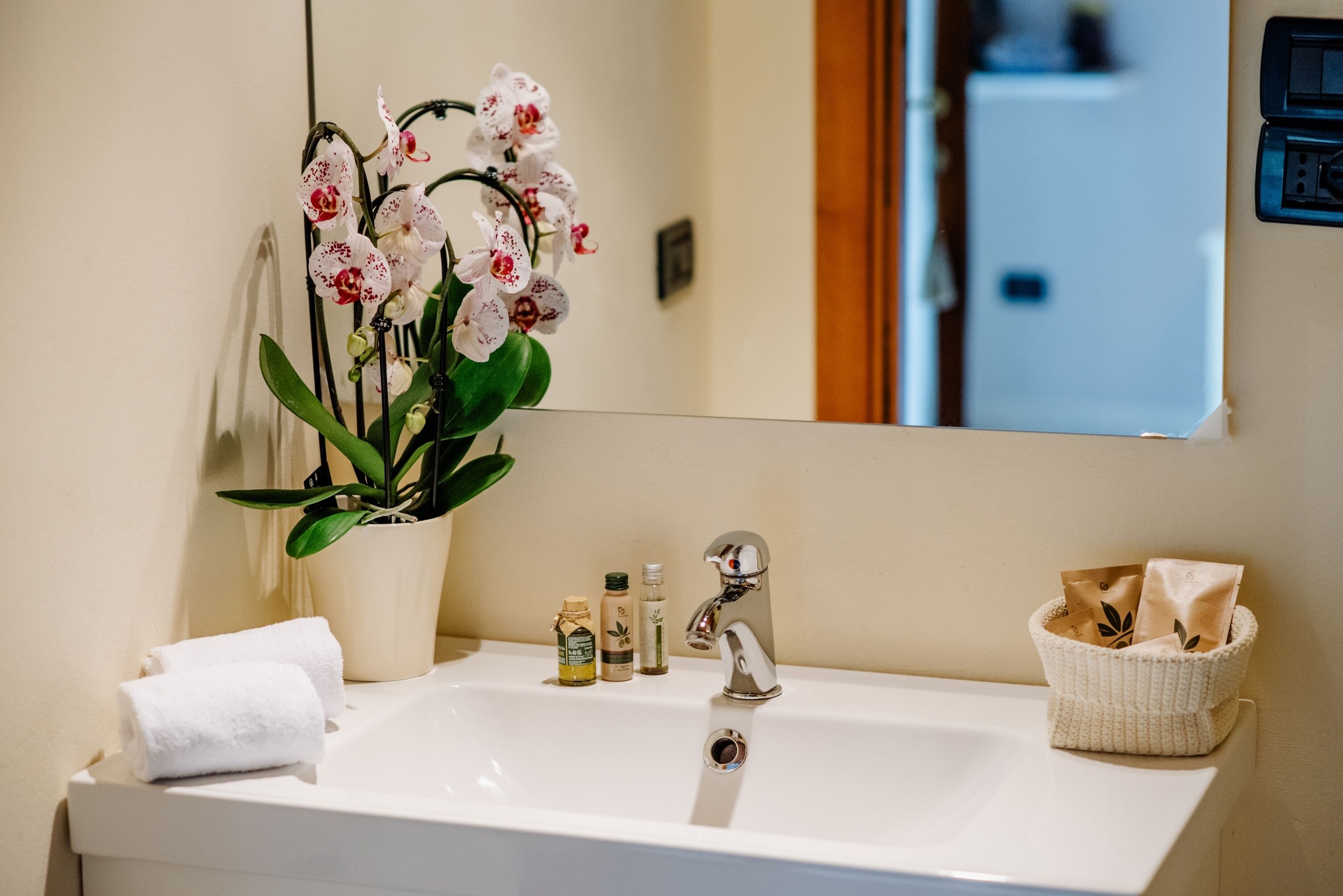 A bathroom sink with a potted orchid, a towel, toiletries, and a basket.