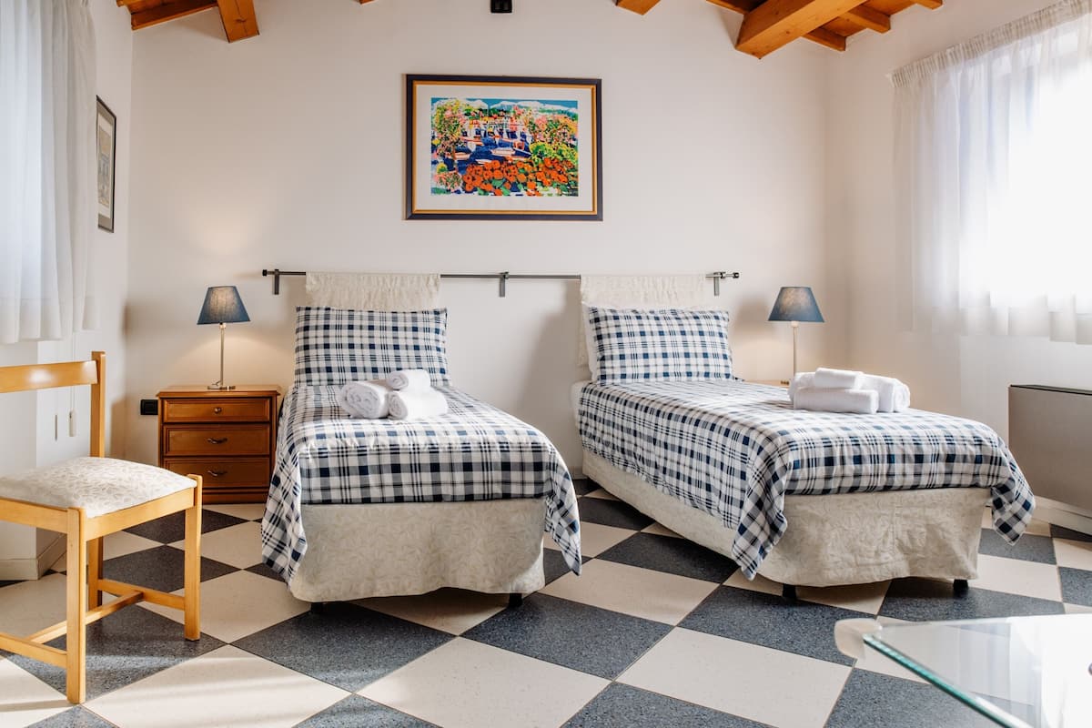 Une chambre avec deux lits, une chaise en bois, une petite table, une table de chevet et un tableau au mur.