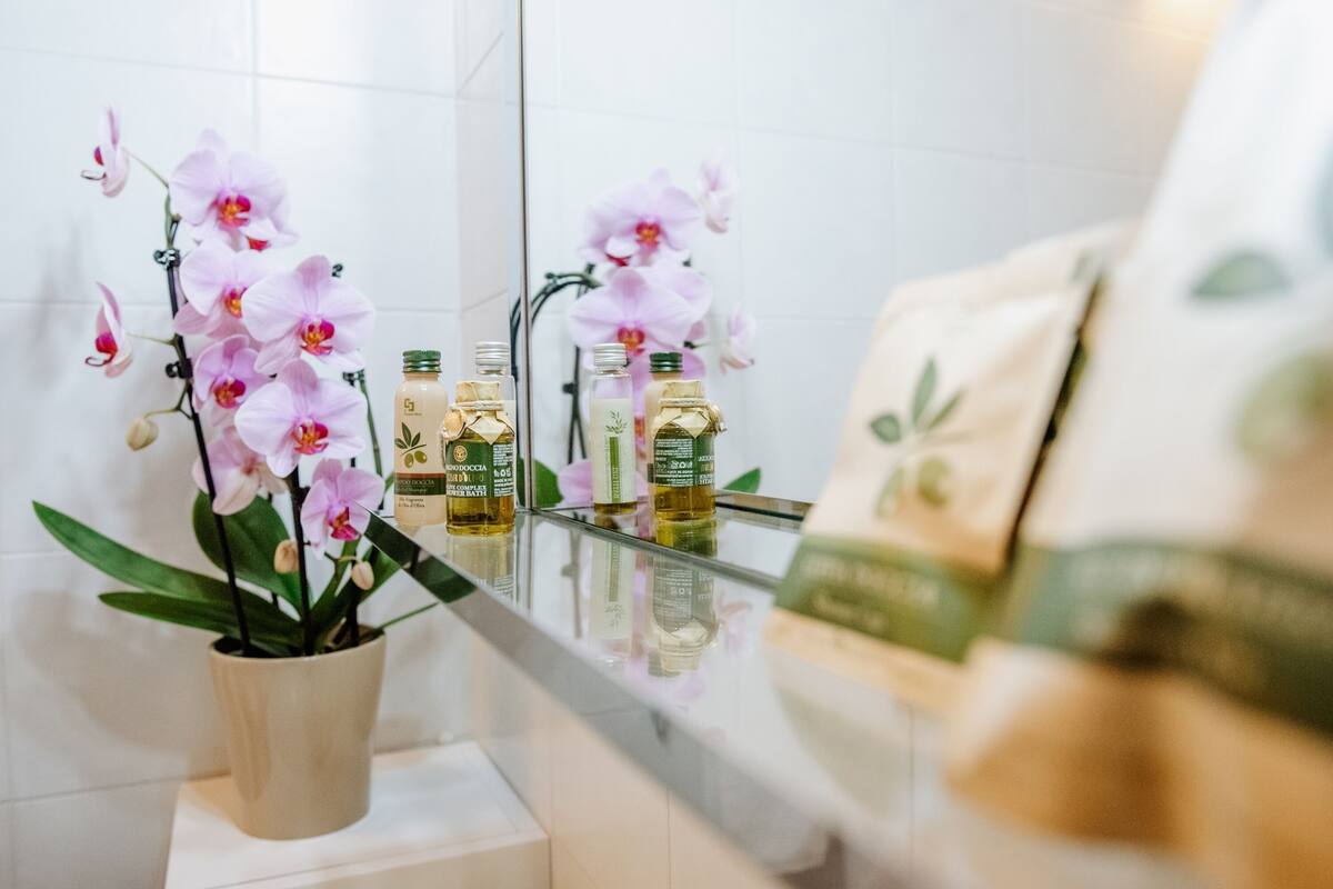 Une salle de bain avec une orchidée en pot, un miroir et des flacons de lotion.