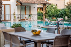 A poolside area with a dining table, chairs, and lounge chairs. - La dolce Vita (Montecchia di Crosara)