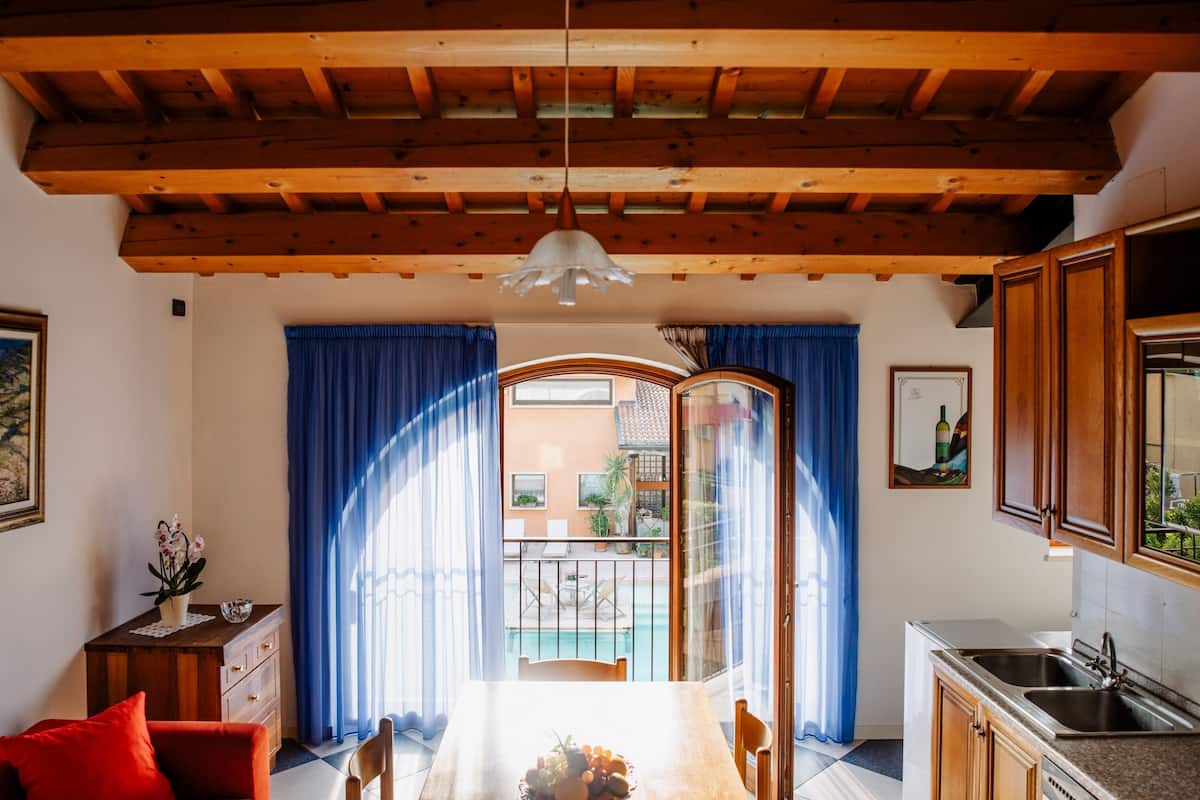 Un coin repas avec un plafond en bois, une table agrémentée d’un centre de table composé de fruits, et une vue sur une piscine et un espace extérieur, visible à travers une porte vitrée.
