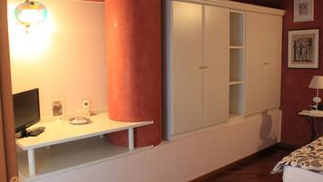 A bedroom with a bed, a desk with a lamp, a wardrobe, and a wall-mounted light fixture.
