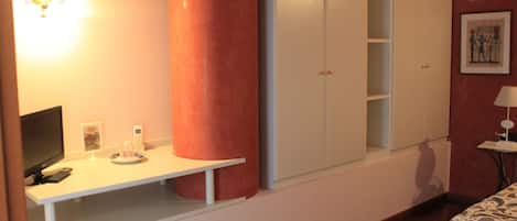 A bedroom with a bed, a desk with a lamp, a wardrobe, and a wall-mounted light fixture.