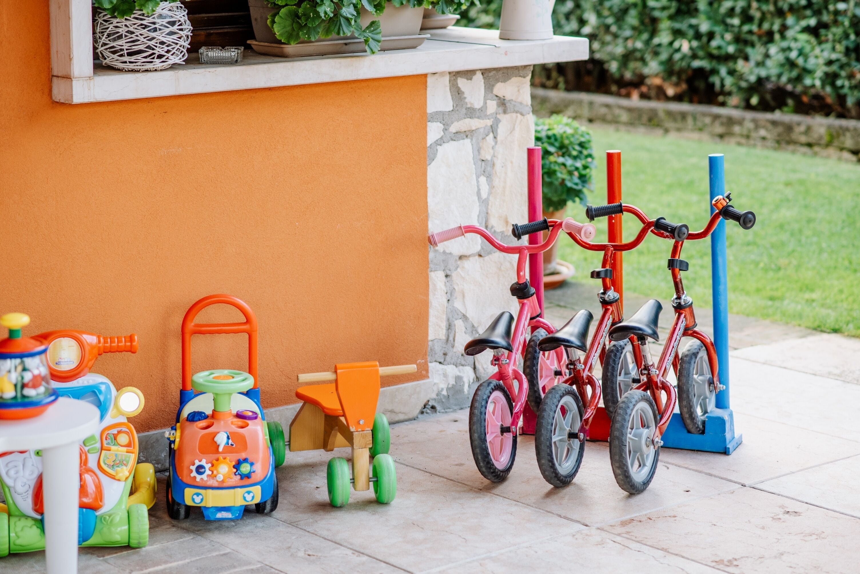 A patio area with a stone wall, a small table with toys, and a red bicycle.