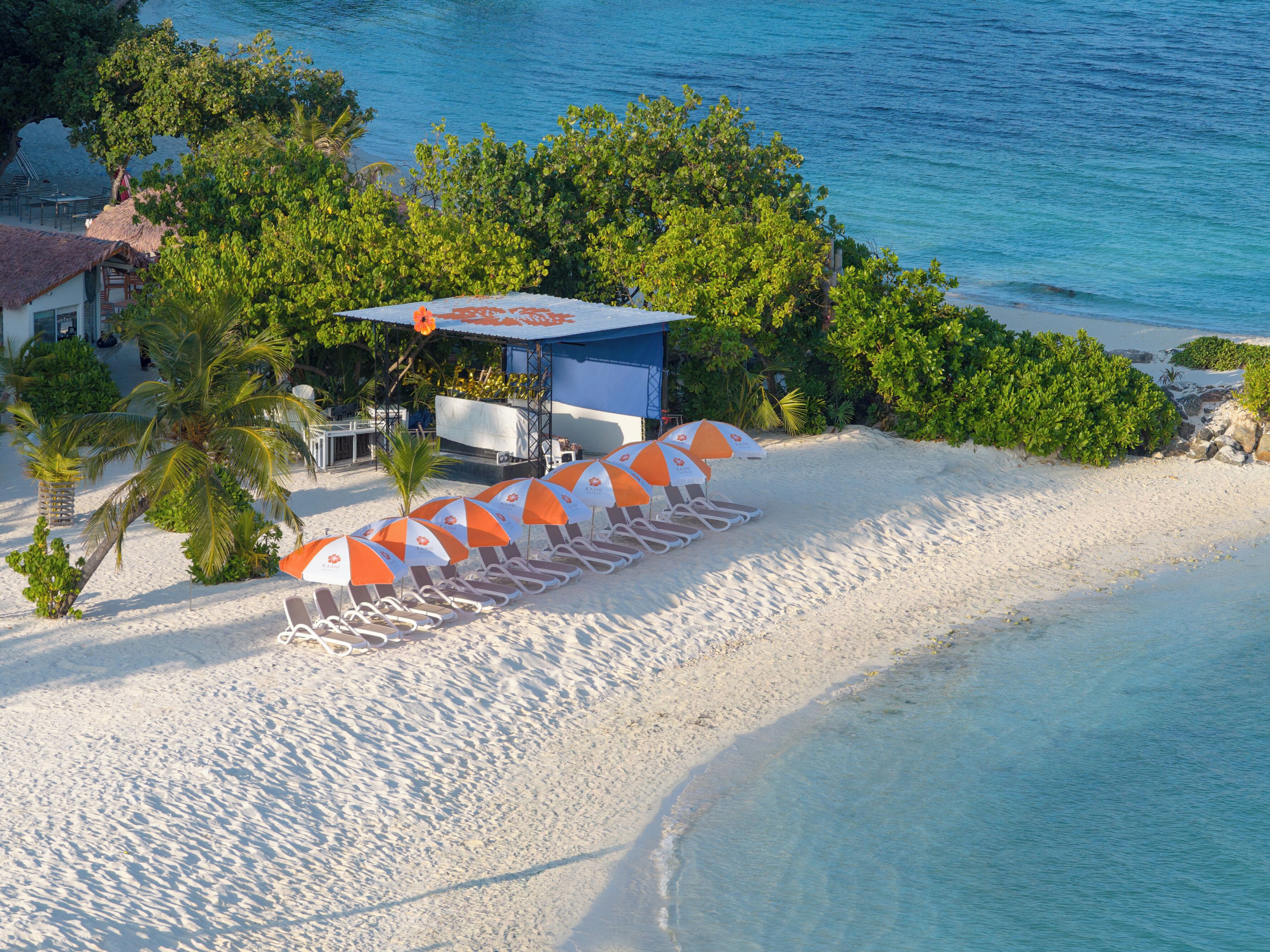 Une plage de sable blanc, un bâtiment bleu et des parasols orange.