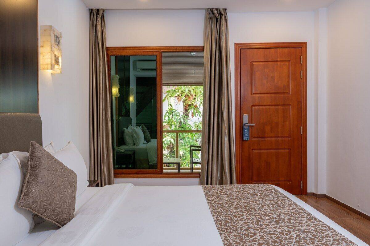 Une chambre d’hôtel avec un lit, une porte en bois et une vue sur un balcon agrémenté de plantes.