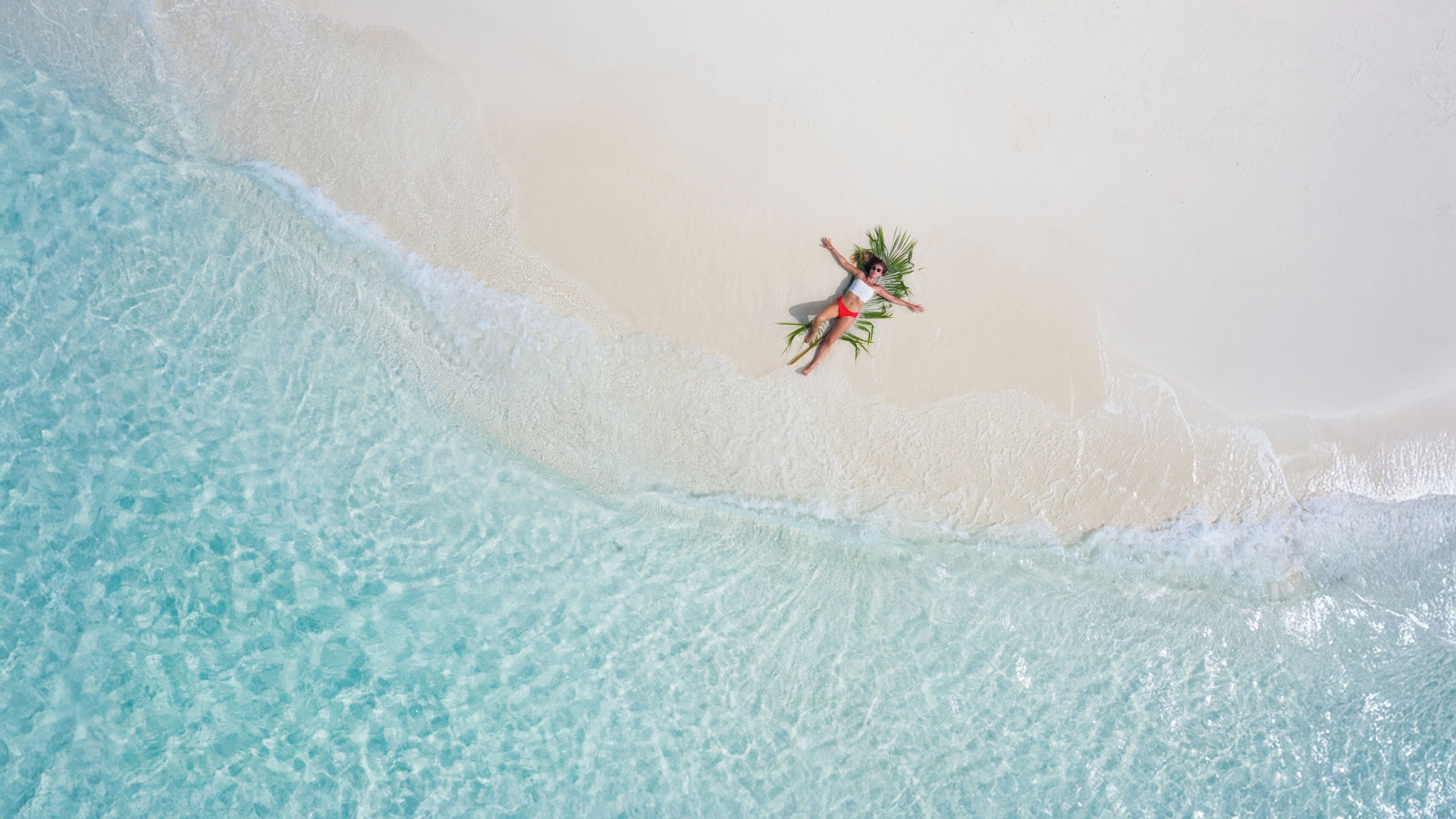 An aerial view of a beach with clear turquoise water and white sand.