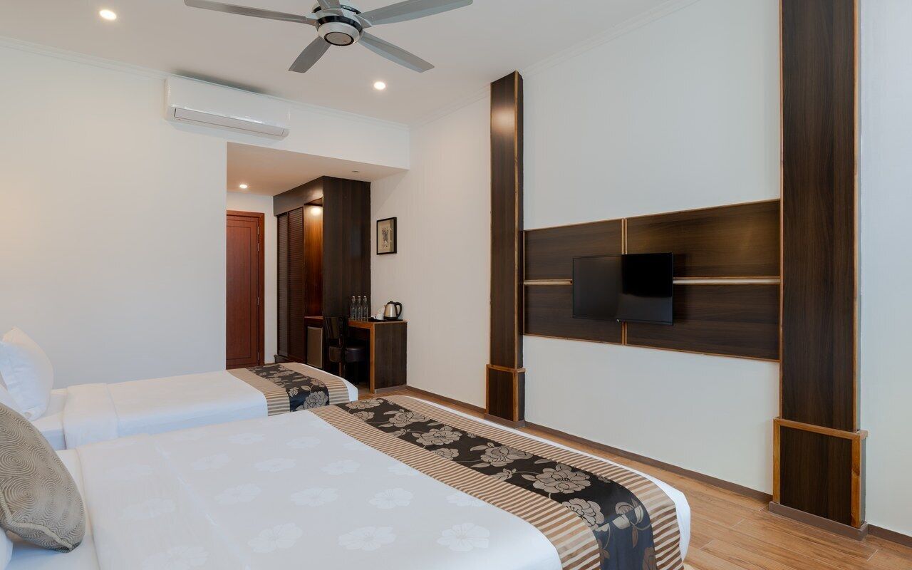 A hotel room with two beds, a ceiling fan, a flat-screen TV, and a wooden headboard.