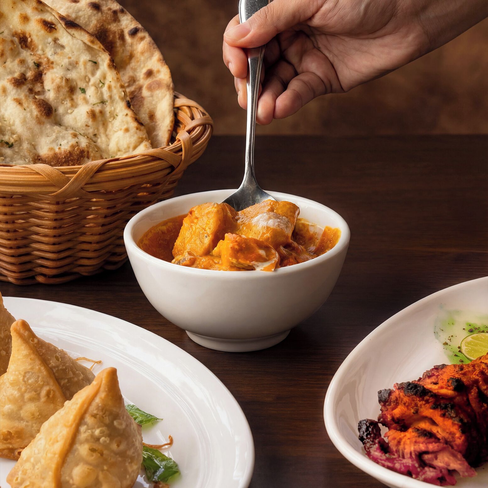 A bowl of curry with naan bread and samosas on a table.
